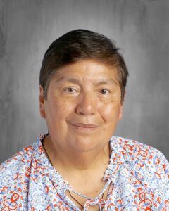 Portrait of a woman with short dark hair wearing a colorful blouse, smiling against a gray background.