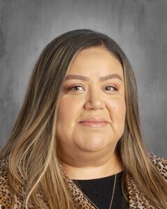 Portrait of a woman with long, wavy hair, wearing a leopard print blouse, against a gray background.