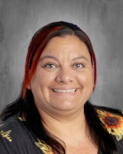 Smiling woman with red and black hair, wearing a floral top, against a gray background.