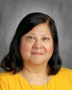 A woman with shoulder-length black hair smiles, wearing a yellow shirt, against a gray background.