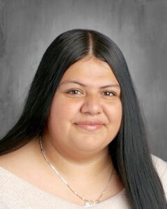 Portrait of a young woman with long black hair, wearing a light sweater and a silver necklace, smiling gently.